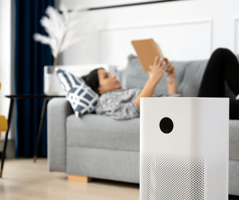 A woman laying on a couch reading a book with an air scrubber in the forefront